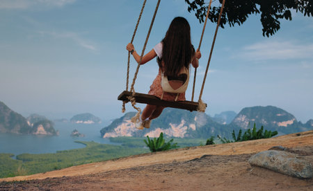 Back view of traveling woman looking on amazing view with cliffs and tropical beach. Freedom and adventure concept.Phang Nga Bay in Samed Nang Chee Viewpoint, Thailand. The girl swings on the swingの写真素材