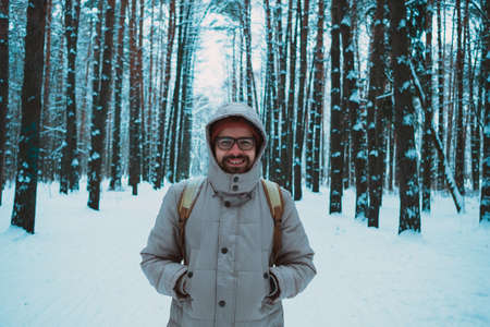 A bearded man in a hat and a backpack stands with his back in winter in a coniferous forest on the river. The concept of winter travel and walks in the woodsの写真素材