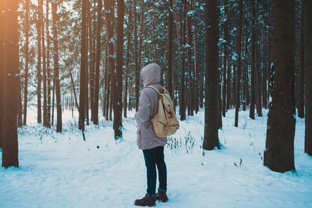 A bearded man in a hat and a backpack stands with his back in winter in a coniferous forest on the river. The concept of winter travel and walks in the woodsの写真素材
