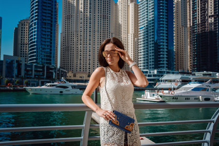 Dubai travel tourist woman on vacation walking on embankment. UAE summer destination. Dubai Marina harbor daylight view. Luxury and comfortable tourism season in UAE. Warm summer day.の写真素材