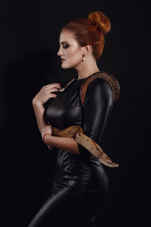 Close up portrait of sexy woman with snake in latex outfit. Redhair model with fashion make up....