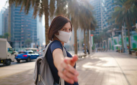 Portrait of young woman wearing in blue dress and white mask for prevent virus, walk in front of skycrapers in modern city. Gesture follow meの写真素材