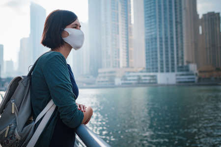 Happy young female traveler with white protective mask in the big city of Dubai, famous place Dubai marina. Luxury and comfortable tourism season in United Arab Emirates. The New Reality and the Normの写真素材