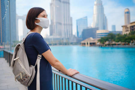 Portrait of beautiful woman wearing a mask for prevent virus walking in Dubai with skyscrapers in the background. Enjoying travel in United Arabian Emirates. Waiting for the evening fountain showの写真素材