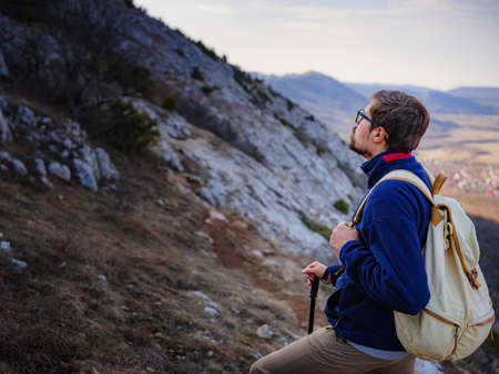 A young man standing on top cliff in spring mountains at sunset and enjoying view of nature. Mountain and coastal travel, freedom and active lifestyleの写真素材