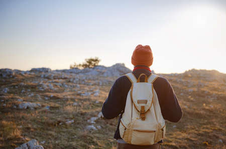 A young man standing on top cliff in spring mountains at sunset and enjoying view of nature. Mountain and coastal travel, freedom and active lifestyleの写真素材