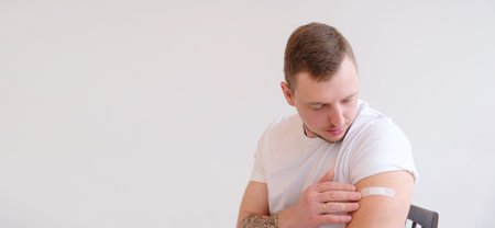 Man in white T-shirt smiling after receiving vaccination on white background. Man showing his arm...