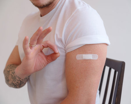 Man in white T-shirt smiling after receiving vaccination on white background. Man showing his arm...