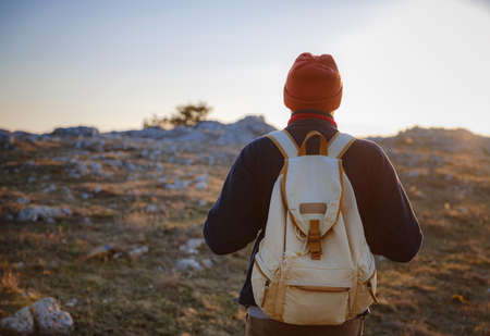 A young man standing on top cliff in spring mountains at sunset and enjoying view of nature. Mountain and coastal travel, freedom and active lifestyleの写真素材