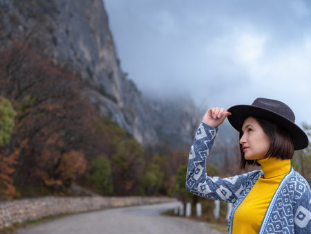 Stylish hipster woman in hat and poncho walking down a mountain road. The concept of travel and wanderlust. An amazing atmospheric momentの写真素材