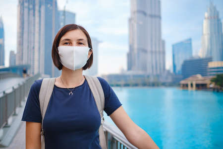 Portrait of beautiful woman wearing a mask for prevent virus walking in Dubai with skyscrapers in the background. Enjoying travel in United Arabian Emirates. Waiting for the evening fountain showの写真素材