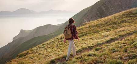A young Asian woman with a backpack hiking in the summer climbing the mountain at sunset. Mountain...