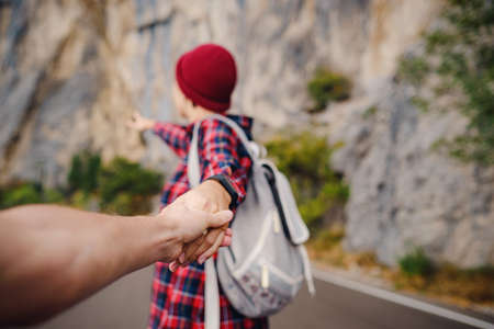 A girl walking down a mountain road on a rainy autumn day. Follow me - POV. Love and travel happy emotions Lifestyle concept. Young family travels active adventurous vacationの写真素材