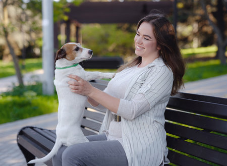 Young woman with her cute Jack Russell Terrier outdoor. Lovely pet. A nice spring evening walk in a green park hugging on a benchの写真素材