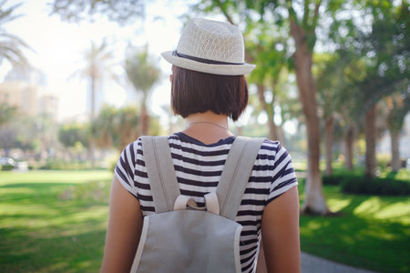 Summer sunny lifestyle fashion portrait of young stylish hipster Asia woman walking on the street, wearing cute trendy outfit and protective mask on face, back viewの写真素材