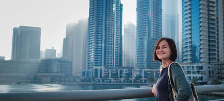 Happy young female traveler in the big city of Dubai, famous place Dubai marina. Luxury and comfortable tourism season in United Arab Emirates.の写真素材