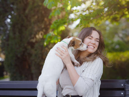 Young woman with her cute Jack Russell Terrier outdoor. Lovely pet. A nice spring evening walk in a green park hugging on a benchの写真素材