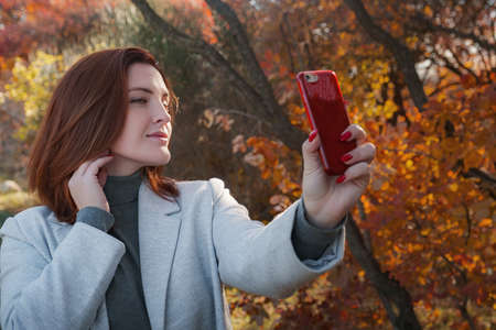 Portrait of a cheerful young woman with autumn leaves in front of the leaves taking selfies. season, technology and people conceptの写真素材