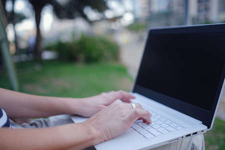 Female hands on laptop, woman types on keyboard sitting in park. Working outside and freelance conceptの写真素材