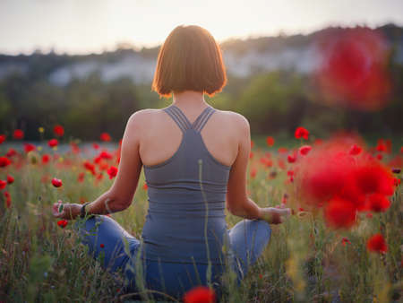 A beautiful woman meditates on a poppy field at sunset. Wellness well-being happiness concept.の写真素材