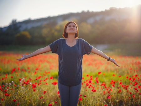 Young beautiful woman with raised arms in spring poppy field. Soft colors. pensive relaxed...