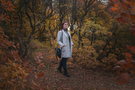 A cute redheaded woman in good spirits poses on an autumn day, enjoying the nice weather. The...