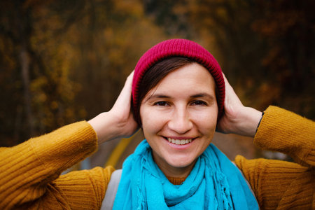 beautiful female hipster in a red hat, yellow sweater and blue scarf walks in the autumn nature. Cool weather. Wanderlust photo series.の写真素材