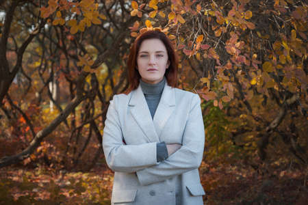 A cute redheaded woman in good spirits poses on an autumn day, enjoying the nice weather. The concept and idea of enjoying autumn and Fall Getawayの写真素材
