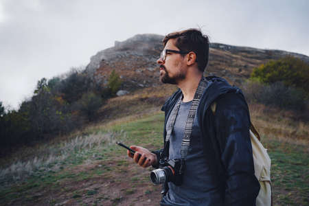 handsome male hipster walks in the autumn nature. Cool weather. He is using mobile phone travel concept. Wanderlust photo series.の写真素材