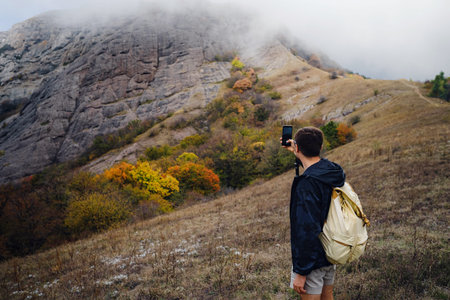 man with backpack and sticks for trekking hiking in the mountains. The beginning of autumn season....
