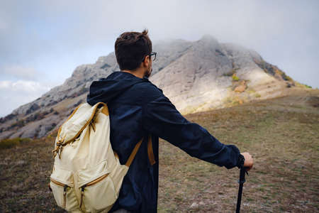 man with backpack and sticks for trekking hiking in the mountains. The beginning of autumn season. Beautiful foggy weatherの写真素材
