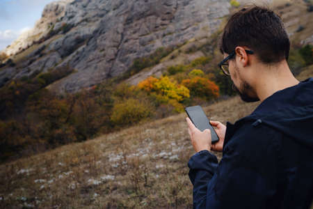 caucasian bearded man traveling in the wild nature using smartphone, with backpack, autumn style, traveler and adventure, free spirit. copy space.の写真素材