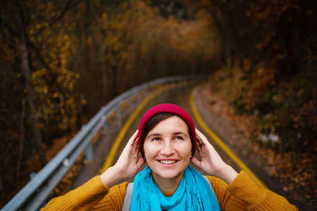 beautiful female hipster in a red hat, yellow sweater and blue scarf walks in the autumn nature. Cool weather. Wanderlust photo series.の写真素材