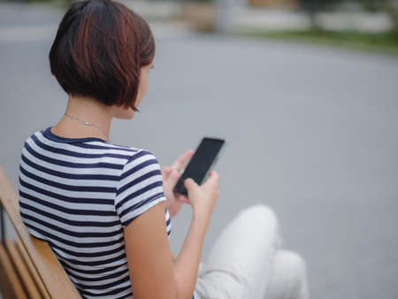 Smiling asian woman using mobile phone in the city street. checking mobile phone. student woman looking at the screen. lady e-learning via her gadgetの写真素材