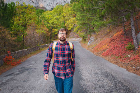 Male hipster Traveler with backpack in plaid shirt and jeans hiking in the mountains travel, trekking in autumn countryside, road in the mountainsの写真素材