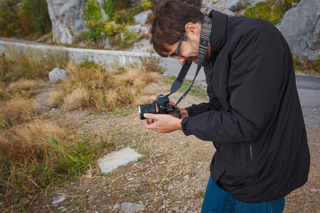 Male hipster Traveler with backpack in plaid shirt and jeans hiking in the mountains travel, trekking in autumn countryside and takes landscape photosの写真素材