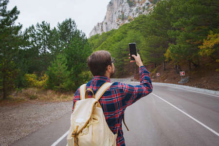 Male hipster Traveler with backpack in plaid shirt and jeans hiking in the mountains travel, trekking in autumn countryside, road in the mountainsの写真素材
