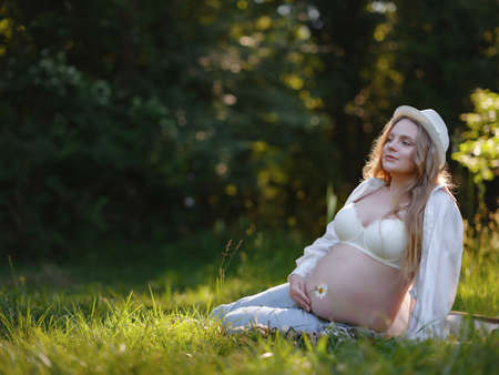 blonde pregnant woman in white shirt and jeans enjoys the silence and beauty of nature. idea of Health and beauty of pregnancyの写真素材