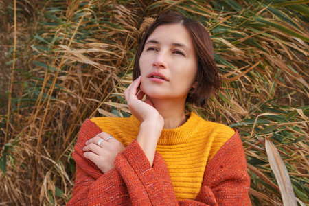 Attractive young woman standing on a windy cold beach wrapped in warm blanket in pampas grass....