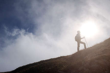 Young woman hiker with backpack on top of mountain on background of blue sky. Walk in the clouds. Discovery Travel Direction Conceptの写真素材