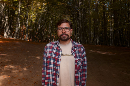 Caucasian hipster male model outdoors in nature. Colorful landscape with trees, rural road, orange and red leaves, sun in autumn.の写真素材