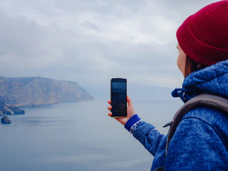 A woman take a photo of the sea on smartphone, female travels along the coast in the cold season. Outdoor. POV. Close upの写真素材