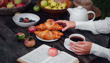 autumn flat lay dark wooden table in garden or on terrace female hands with coffee, apples, croissants, plums and book. idea and concept of warm autumn, cozy lifestyle and sustainability simple lifeの写真素材