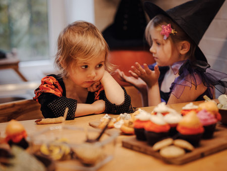 halloween holiday and childhood concept. Happy Family preparing for Halloween. two sisters taste decorated cookies at kitchen.の写真素材