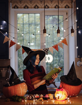 All hallows eve. woman in witch costume and hat read book, glowing jack o lantern carved pumpkin on the table, with Halloween decorations in dark roomの写真素材