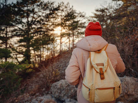 man with backpack and red hat hiking in the sunset mountains stands on rocky hiking trail or path. Cold weather. Winter hike. Outdoor vibes and adventures wanderlustの写真素材