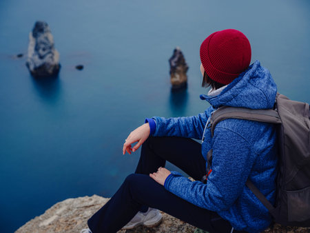 Back view of woman in blue jacket and hat on shore of North sea on cold winter day. Mood Scandinavian weather. travel adventure lifestyle idea and conceptの写真素材