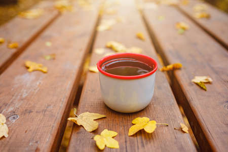 Cup of tea with autumn leaves reflection on wooden table. Season of autumn walk. fall still lifeの写真素材