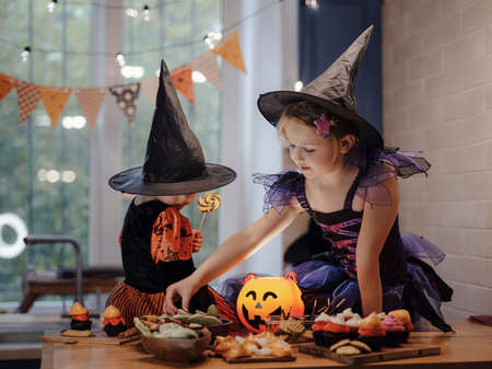 halloween holiday and childhood concept. Happy Family preparing for Halloween. two sisters taste decorated cookies at kitchen.の写真素材