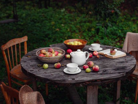 beautiful autumn still life in apple orchard, old table with cup, teapot, apples and book. Fall Getaway, Apple Picking anf Harvest Day Celebration conceptの写真素材